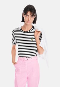Black and white striped t-shirt featuring a small pineapple embroidery, paired with pink trousers that have a belted waist and pockets.