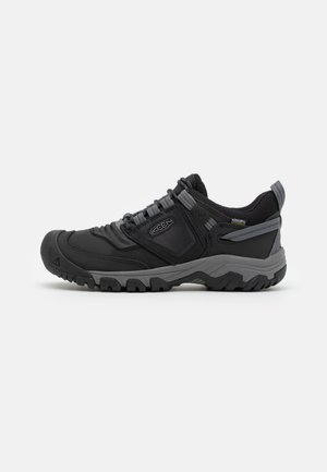 Schwarzer und grauer niedriger Wanderschuh mit robustem Profil, Mesh-Obermaterial, Schnürverschluss und Zuglasche an der Ferse.