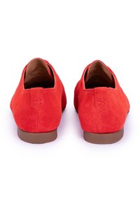 Zapatos rojos de ante con un acabado suave, parte trasera redondeada y un pequeño tacón. Presentan laterales troquelados y una plantilla texturizada para mayor comodidad.