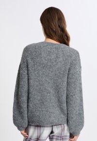 Maglione grigio lavorato a maglia con un motivo testurizzato, spalle scese e maniche lunghe. Il retro presenta un collo rotondo e una vestibilità morbida.