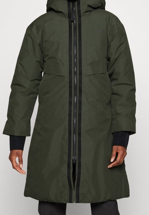 Dark green long winter coat with black zipper and hood, worn by person showing hands and lower arms.