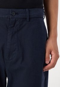 Navy blue, lightweight fabric trousers featuring a button closure, side pockets, and a smooth texture, with a tailored fit.