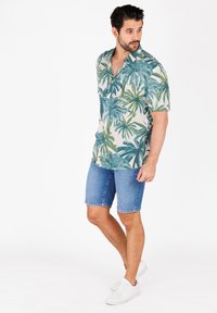 Kurzärmeliges Hemd aus leichtem Material mit grün-blauem Palmblattmuster, kombiniert mit Jeansshorts und weißen Sneakers.