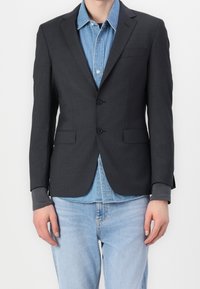 Dunkelgrauer Blazer aus strukturiertem Stoff mit zwei Knöpfen, aufgesetzten Revers und Fronttaschen, getragen über einem hellen Denimhemd.