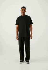 T-shirt preto de mangas curtas combinado com calças largas pretas. Modelo usando óculos de sol com tonalidade dourada e sapatilhas pretas exibe um estilo minimalista.