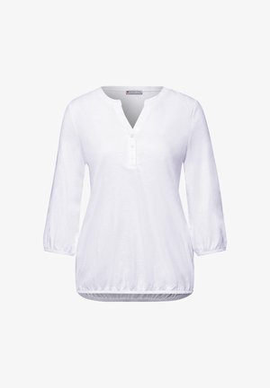 Blouse blanche pour femme avec manches trois-quarts, col en V à trois boutons, et ourlet élastique, présentée sur un fond blanc.