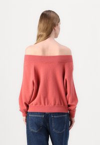 Pull corail à épaules dénudées avec un col et des poignets côtelés, arborant une coupe décontractée. Assorti à un jean en denim foncé taille haute.