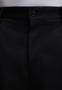 Schwarze Hose aus glattem Stoff mit flachem Frontteil, einfacher Knopfverschluss und ordentlich genähten Nähten.