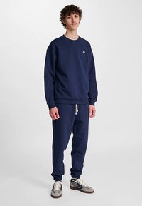 Mörkblå sweatshirt och sweatpants-set i mjukt tyg, med rund hals, ribbade mudd och ett broderat märke på bröstet.