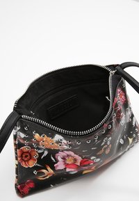 Černá taštička s květinovým vzorem, ozdobená stříbrnými cvočky, se zipovým uzavřením a jedním popruhem. Uvnitř je podšita texturovanou černou látkou.