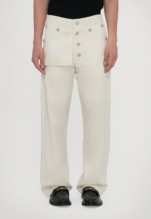 White wide-leg trousers made of smooth fabric with decorative silver buttons and a pocket flap detail. Worn with black loafers.
