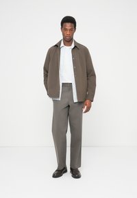 Καφέ σακάκι με κουμπιά πάνω από ένα ανοιχτό γαλάζιο πουκάμισο με κουμπιά, συνδυασμένο με ανοιχτό γκρι παντελόνια και σκούρα παπούτσια. Απλός και μοντέρνος σχεδιασμός.