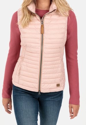 Femme portant une veste matelassée rose clair zippée sur un haut à manches longues couleur rose poussière et un jean bleu, vue du cou aux hanches.