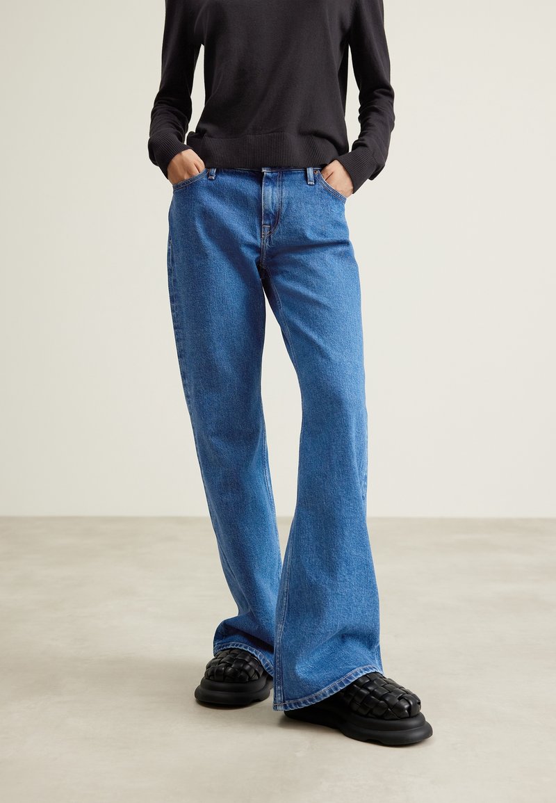 Blue denim wide-leg jeans with a high waist, featuring a standard five-pocket design and contrasting stitching. Paired with black textured shoes.