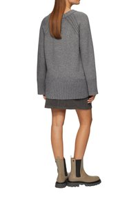 Pull en tricot gris avec un ourlet et des poignets côtelés, associé à une jupe gris foncé et des bottines beiges à bout noir avec des panneaux élastiques sur les côtés.