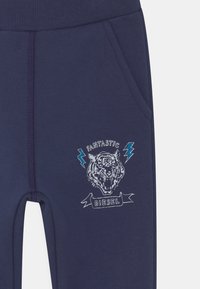 Calças de moletão azul-marinho com uma cintura canelada, apresentando um gráfico de um tigre e o texto "FANTASTIC DIESEL" em detalhe bordado.