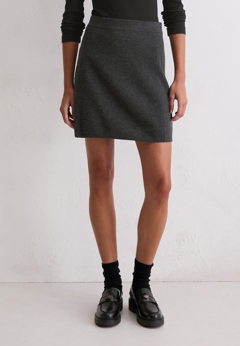 Hógrauwe A-lijn rok van zachte stof, met een soepele taille en een eenvoudig, strak design. Gepaard met zwarte instappers en sokken.