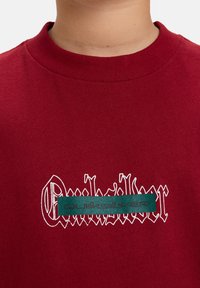 Bordeaux katoenen t-shirt met een ronde halslijn. Bevat een wit scriptlogo en een groene rechthoekige accent met de merknaam in het wit.