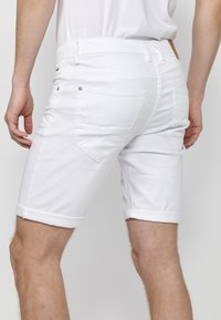 Bermudas de mezclilla blanca con dobladillos enrollados, cinco bolsillos y detalles de costura sutiles. Textura suave, corte moderno y sin herrajes visibles.