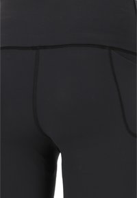 Musta legginsit sileällä pinnalla, joissa on tasasaumat ja tasku sivulla. Suunnittelu on yksinkertainen ja vartalonmyötäinen.