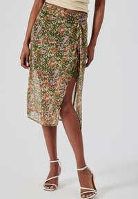 Jupe wrap florale verte, ornée de motifs orange, rose et violet. Tissu léger et transparent avec une fente haute et un système de fermeture à lien ajustable.