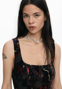 Must ja punane sametkleit ruudukujulise kaelusega, millel on kuldsed täpid. Hõbedast kettkaelakee keeruka disaini ja peegeldavate detailidega.