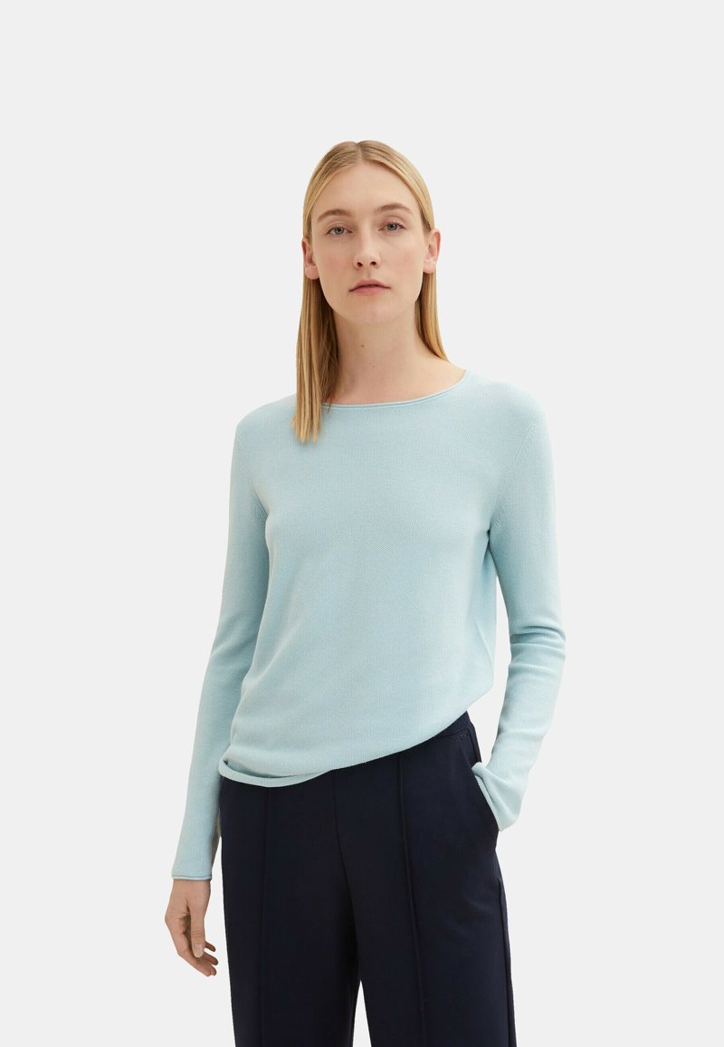 Light blue long-sleeve sweater with a crew neckline, textured knit pattern, and slightly relaxed fit, paired with dark trousers.