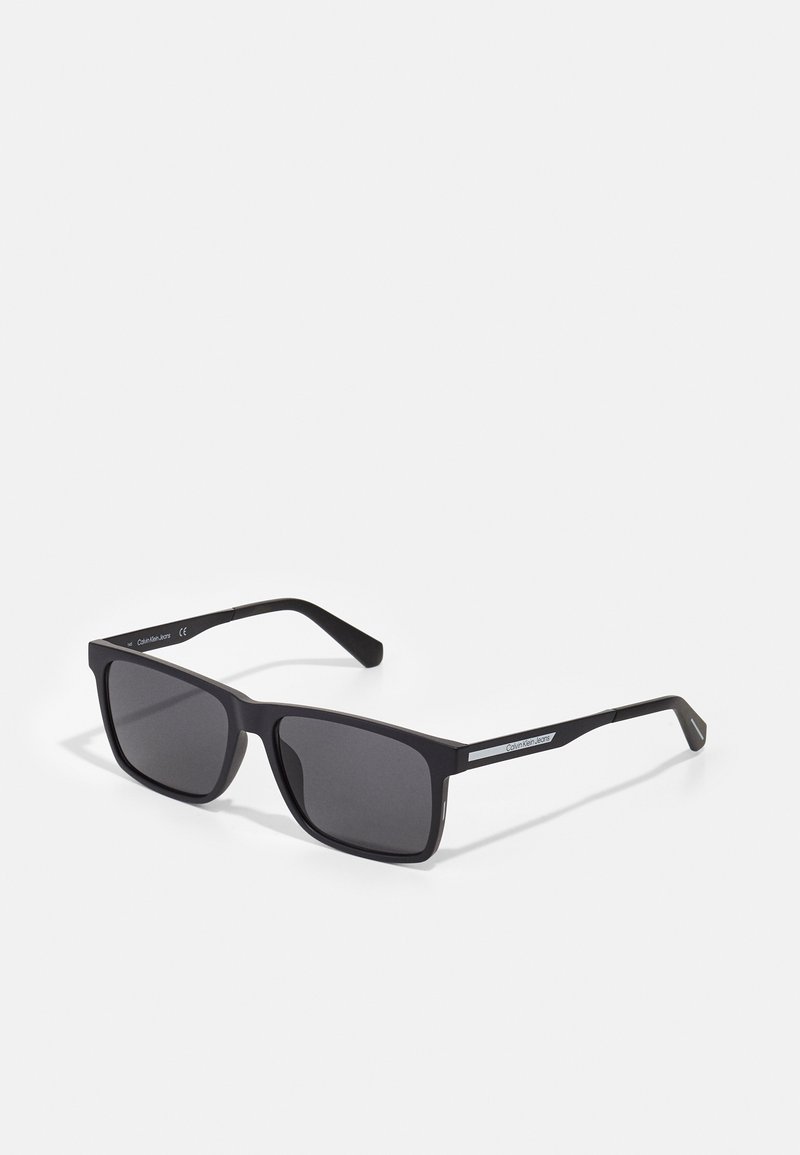 Black square sunglasses with dark lenses and a matte finish. Features slender temples with a silver accent on one side.
