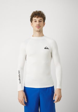 Hvit langermet rashguard laget av elastisk materiale, med en svart logo på brystet og "Quiksilver" tekst på ermene.