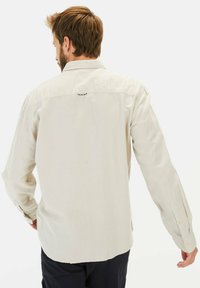 Lichtbeige overhemd met lange mouwen, een button-down kraag en knoopmanchetten. Heeft een subtiele textuur en een klein lusdetail aan de achterkant.