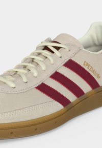 Baskets en daim beige avec trois bandes bordeaux, semelle en gomme, lacets blancs et marquage "Spezial" doré sur le côté.