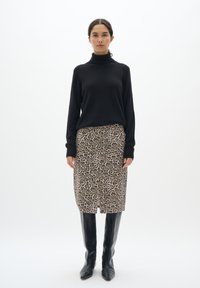 Črn turtleneck pulover v kombinaciji z krilom do kolen s leopardjim vzorcem in črnimi čizmi do kolen, na beli podlagi.