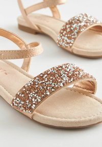 Sandali in rosé con tomaia texturizzata e una fascia ampia decorata con strass trasparenti e bronzo. Design piatto e open-toe.