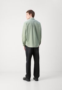 Cămașă din fustă verde deschis, cu mâneci lungi, manșete cu butoni și un tiv ușor curbat. Purtați-o cu pantaloni negri drepti și pantofi negri.