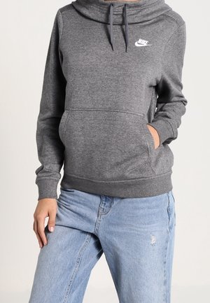 Grauer Nike-Hoodie mit einem Schalkragen, Fronttasche und gerippten Bündchen. Verfügt über ein kleines weißes Logo auf der Brust. Kombiniert mit hellblauen, distressed Jeans.