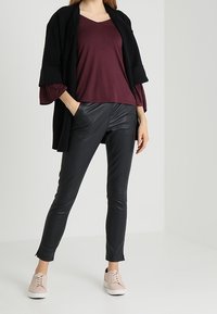 Black open jacket over a burgundy top, paired with black faux leather pants and light pink sneakers. Smooth textures, casual design.