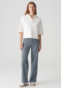 Weißes Kurzarm-Polohemd mit V-Ausschnitt, kombiniert mit hoch taillierten, marineblauen und weißen gestreiften Weitbein-Hosen. Graue Sneakers runden den Look ab.
