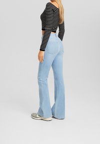 Vaqueros de campana azul claro con un ajuste ceñido en la parte trasera, combinados con un top corto de manga larga a rayas en blanco y negro. Textura de denim suave y diseño clásico.