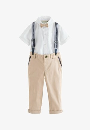 Camisa blanca de manga corta con botones, pajarita beige y pantalones beige con tirantes azul marino y puños doblados.