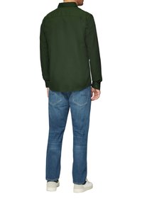 Groen overhemd met lange mouwen en knoopmanchetten, gedragen met lichtblauwe jeans en witte sneakers. Glad materiaal en klassiek kraagontwerp.