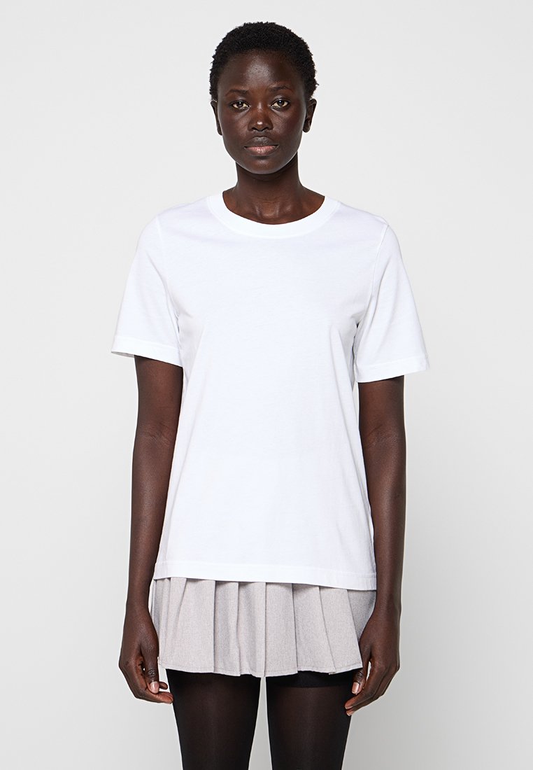 Biała bawełniana koszulka z krótkim rękawem i okrągłym dekoltem. Połączona z szarą spódnicą plisowaną i czarnymi rajstopami. Prosty, nieozdobiony design.