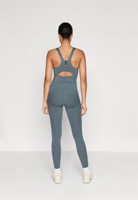 Tyrkysový športový set s dizajnom výrezov na chrbte v podprsenke a vysokými legínami, vyrobený z pružného a hladkého materiálu.