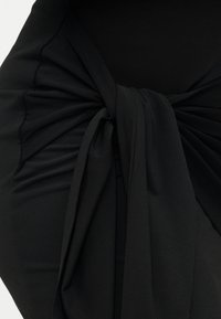 Μαύρο ύφασμα ενδύματος με λεπτομέρεια στριμμένου κόμπου στη μέση, με απαλή υφή και ομαλή επιφάνεια, δημιουργώντας ένα εφέ πέπλου.