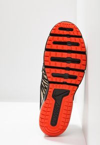 Semelle de chaussure de sport noire et orange avec un motif de semelle distinctif, présentant du caoutchouc texturé et la marque Nike Air Max.