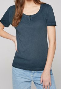 Tmavě modré tričko s krátkými rukávy, zakulaceným výstřihem a třemi knoflíkovými detaily na hrudi, vyrobené z jemné, hladké tkaniny.
