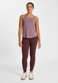 Débardeur lavande sans manches avec fines bretelles et ourlet arrondi, assorti à un legging bordeaux. Le mannequin porte des baskets blanches avec des accents marron.