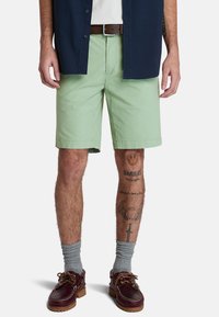 Jasnozielone szorty wykonane z bawełny, z płaskim przodem i bocznymi kieszeniami, w połączeniu z granatową koszulą na guziki i brązowym paskiem.