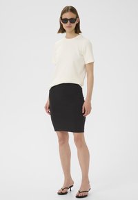 Top alb cu mâneci scurte, combinat cu o fustă tip creion neagră, ajustată, și flip-flops negri cu toc; texturi fine, design minimalist.