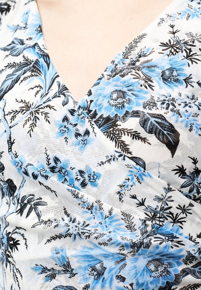 Κοντινή λήψη λευκού υφάσματος με μπλε και μαύρο ανθικό σχέδιο, που δείχνει V-λαιμόκοψη σε ένδυμα που φοριέται από ένα άτομο.