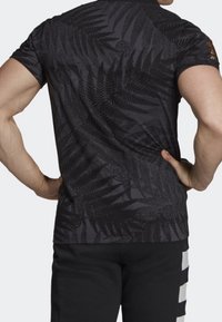 Svart kortärmad skjorta med ett texturerat mönster av ormbunke, med en slät tygfinish och en figurnära design.